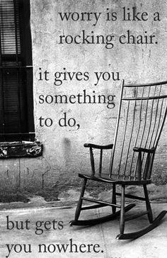 a wooden rocking chair sitting on top of a sidewalk next to a wall with a quote