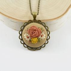 "This embroidered peony necklace in gorgeous shades of coral, ecru and yellow is just gorgeous! Whether you are looking for an awesome gift, or are looking for something pretty for yourself, you just can't go wrong with this gorgeous botanical pendant. The flowers are embroidered on a tan cotton background. The flowers are embroidered in gorgeous hues of coral, ecru, and yellow. Description in a nutshell: -Zinc Alloy pendant and chain with a beautiful antique bronze finish for a gorgeous antique Cottagecore Necklace, Coral Peony, Embroidered Brooches, Embroidered Buttons, Shades Of Coral, Lavender Necklace, Romantic Anniversary Gifts, Coral Peonies, 2nd Anniversary Gift