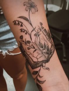 a woman's arm with a book and flowers tattoo design on the left forearm