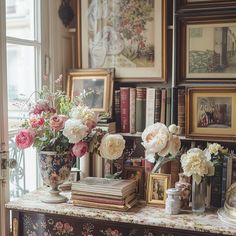 there are many vases with flowers on the table in front of books and pictures