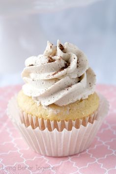 a cupcake with white frosting and sprinkles sitting on a pink tablecloth