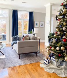 a living room with a christmas tree in the corner and blue curtains on the windows