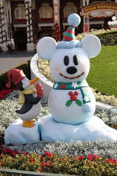 mickey mouse and penguin snowman statue in front of the disneyland world christmas village entrance