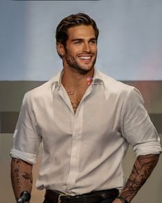 a man with tattoos standing in front of a microphone and smiling at the camera while wearing a white shirt