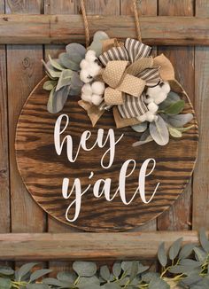 a wooden sign that says hey y'all hanging on a wall with greenery