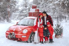 a man and woman standing next to a red car in the snow with two children