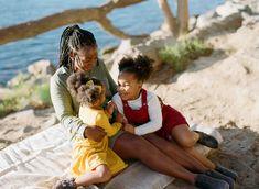 two women and a child are sitting on the sand by the water with their arms around each other