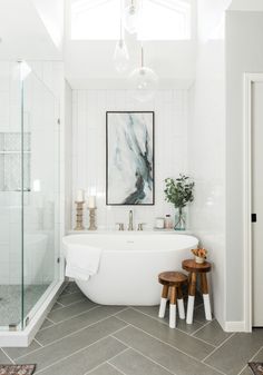 a white bath tub sitting under a window next to a wooden table with two stools