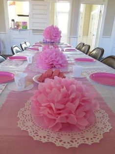 the table is set with pink flowers and place settings for people to sit down at