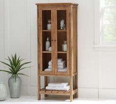 a wooden cabinet sitting next to a potted plant on top of a white floor