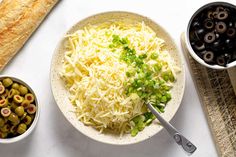 a bowl filled with cheese next to bowls of olives and bread