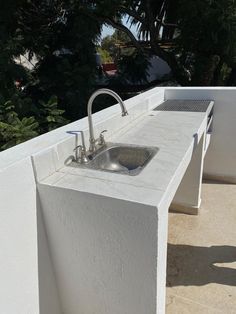 an outdoor sink with two faucets on the outside wall and trees in the background