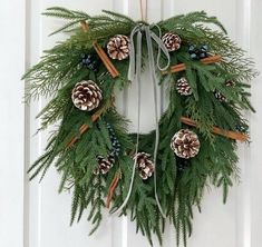 a wreath with pine cones and cinnamon sticks hanging on the front door, decorated with greenery