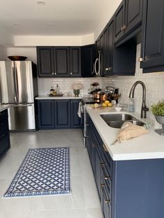 a kitchen with blue cabinets and white counter tops is pictured in this image, there are two rugs on the floor next to the sink