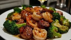 a white plate topped with shrimp and broccoli next to a glass of wine