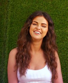 a woman with long hair standing in front of green grass and smiling at the camera