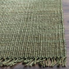 a green rug with fringes on top of a wooden floor in an empty room