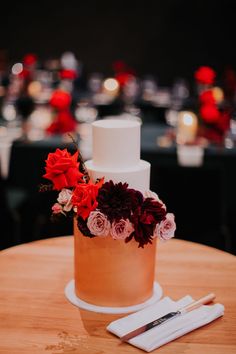 a wedding cake with red and pink flowers on it sitting on a table next to napkins