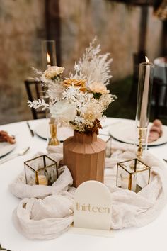 a white table topped with a vase filled with lots of flowers next to two candles