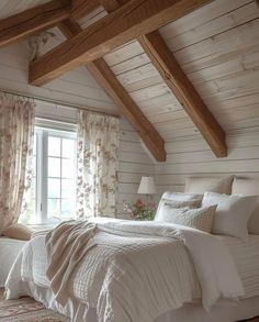 a white bed sitting under a window in a bedroom next to a wooden beamed ceiling