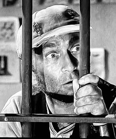 a man is looking through the bars of a jail cell with his hat on and eyes wide open