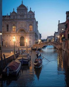 several small boats are docked in the water near some buildings and lights at night time