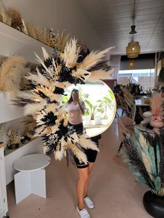 a woman is standing in a room with feathers on her head and holding a mirror