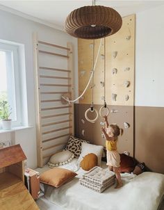 a young child playing on a bed in a room with climbing walls and toys hanging from the ceiling