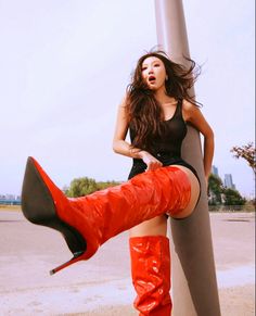 a woman in red boots leaning against a pole with her leg up on the pole