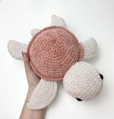 a hand holding a pink and white crocheted turtle toy with its head on it's back