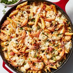 a skillet filled with pasta and shrimp next to a bowl of parmesan cheese