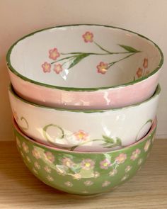 three bowls are stacked on top of each other with flowers painted on the sides and green rims