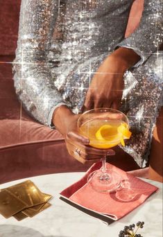 a woman in sequins holding a cocktail glass with an orange slice on it