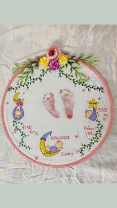 a hand and foot print on a white cloth with pink trim around the feet, surrounded by flowers