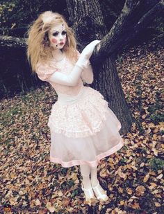 a woman dressed up as a zombie holding onto a tree in the woods with leaves all around her