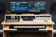 a desk with two computer monitors, keyboard and speakers next to each other in front of a black wall