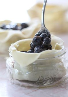 a spoon full of blueberries and cream in a glass jar on a counter top