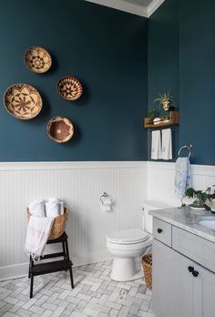 a white toilet sitting next to a bathroom sink under three baskets on the wall above it