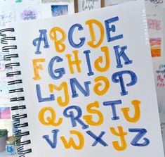 an open notebook with the letters drawn on it in blue, yellow and orange ink