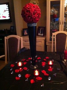 a black table with red roses in a vase and candles on the table next to it