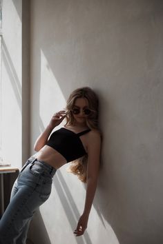 a woman leaning up against a wall with her hand on her hip and wearing sunglasses