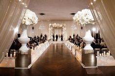 the aisle is lined with white flowers and vases for an elegant wedding ceremony venue