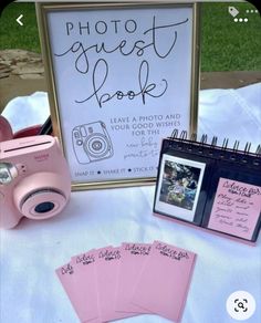 a table topped with pink cards and a camera next to a sign that says photo guest book