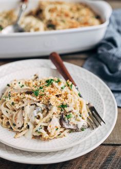 a white plate topped with pasta covered in mushrooms and parmesan cheese next to a casserole dish