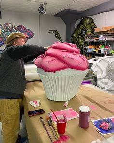 a man standing next to a giant cupcake covered in pink frosting