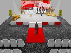 a man is standing on a red carpet in front of a stage with white chairs