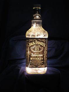 an illuminated bottle of jack daniels whiskey sitting on a black cloth covered table with dark background