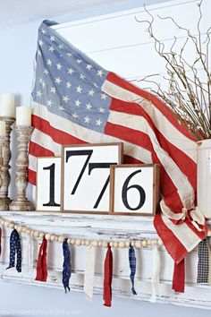 an american flag and wooden blocks with the number seventy six on them are hung above a mantle