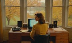 a woman sitting at a desk with a computer in front of her, looking out the window