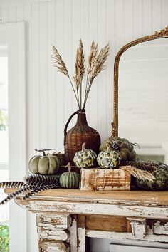 an old table with pumpkins and gourds on it in front of a mirror